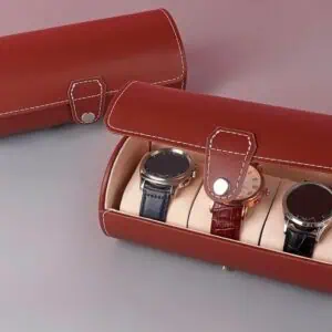 The Watch Travel Roll Case Brown Three spaces, featuring white stitching, securely holds three wristwatches on separate cushions. A second closed case sits beside it on a grey and mauve surface.