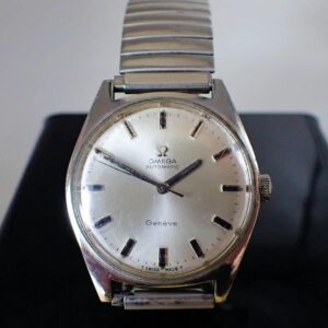 The Omega Genève Automatic Wristwatch features a silver dial, minimalist hour markers, and a metal link strap, beautifully presented against a dark background.