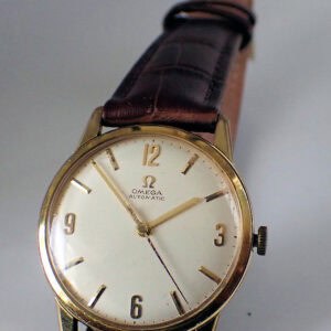 The OMEGA Automatic Gold Plated Watch 1961 features a round gold case, white dial, gold hour markers, and a brown leather strap, displaying the time as 4:16.