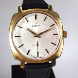 The Zenith Gold Plated Presentation Watch 1970s features a white dial with black hour markers, gold hands, a sub-dial above 6 o’clock, the Zenith logo, Swiss Made at the bottom, and a black leather strap.