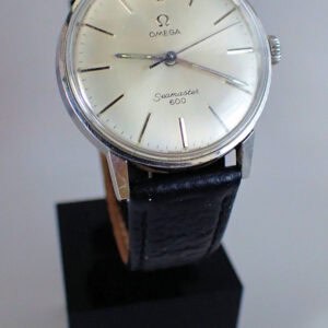 An Omega Seamaster 600 with Silvered Dial from 1966, featuring a black leather strap and minimalist hour markers, displayed on a black stand.