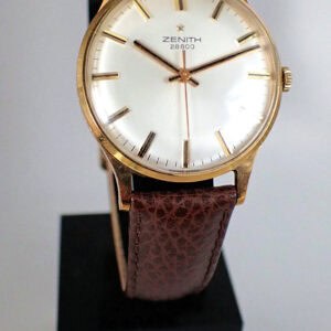 A Zenith 28800 Mechanical Solid 9ct Gold Watch with a white dial, gold hour markers, and brown leather strap is displayed on a black stand against a plain background.