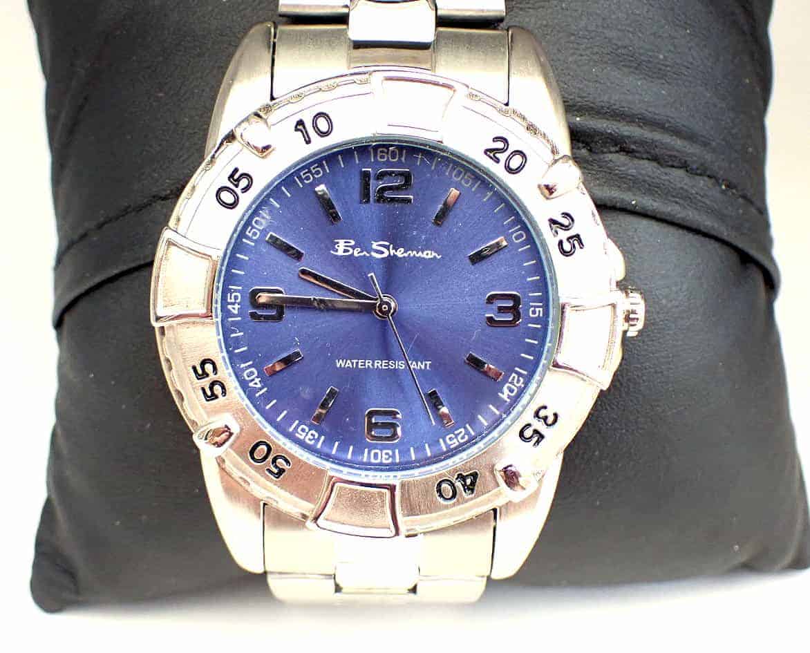 The Ben Sherman Men's Blue Dial Silver Colour Bracelet Watch features a silver metal strap, blue dial with silver hour markers and hands, minute-marked bezel in five-minute increments, and is displayed on a black cushion.