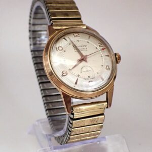 A Genève 1950s 25 Jewels Automatic Watch with a vintage gold-tone case, round face, silver dial, Arabic numerals, and metal expandable strap is displayed upright on a clear stand against a light background.