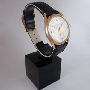 The Inventic Mechanical Circa 1965 - Bargain Basement! features a gold case, white dial, and black leather strap, showcased on a black stand with a plain background.