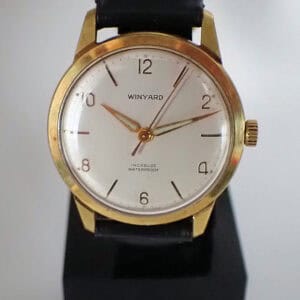 A gold Winyard Hand Wound Incabloc wristwatch with a white dial, black hour markers, and black leather strap, displaying 10:11:36 and the words INCABLOC WATERPROOF on the face.
