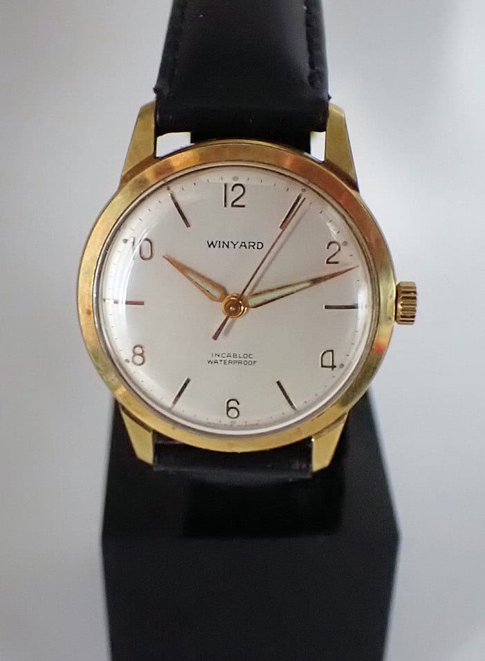 A gold Winyard Hand Wound Incabloc wristwatch with a white dial, black hour markers, and black leather strap, displaying 10:11:36 and the words INCABLOC WATERPROOF on the face.