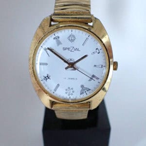 The Spezial Masonic Mechanical Wristwatch features a vintage gold case, white dial with black line drawings of tools and household items as hour markers, the "Spezial" label, and a matching metal strap.