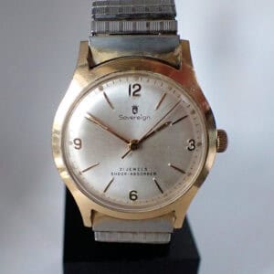 A vintage Sovereign 21 Jewel Mechanical wristwatch with a gold-tone case, silver dial featuring Arabic numerals at 12, 3, 6, and 9, metal strap, and dial marked "Sovereign," "21 Jewels," and "Shock-Absorber.