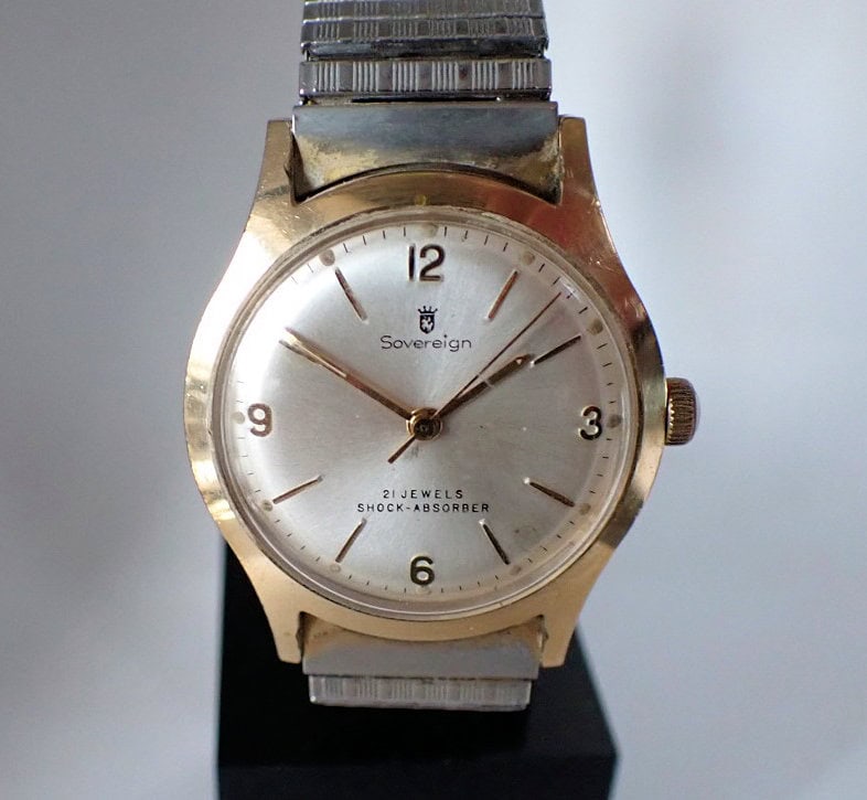 A vintage Sovereign 21 Jewel Mechanical wristwatch with a gold-tone case, silver dial featuring Arabic numerals at 12, 3, 6, and 9, metal strap, and dial marked "Sovereign," "21 Jewels," and "Shock-Absorber.