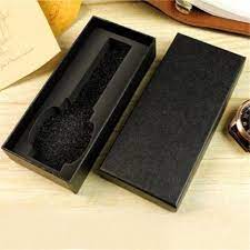 A Fitted Watch Box, black and rectangular with its lid off, reveals a foam insert shaped for a wristwatch. It rests on a light wooden surface with the watch and papers alongside.