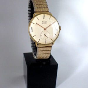 An Avia Incabloc 17 Jewels Mechanical Swiss Made wristwatch with a gold-tone metal strap and round face, shown upright on a black stand against a plain white background. Features simple hour markers and a small seconds sub-dial.