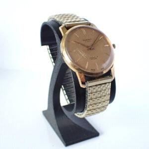 Gold vintage wristwatch with stainless steel mesh bracelet displayed on a black stand.