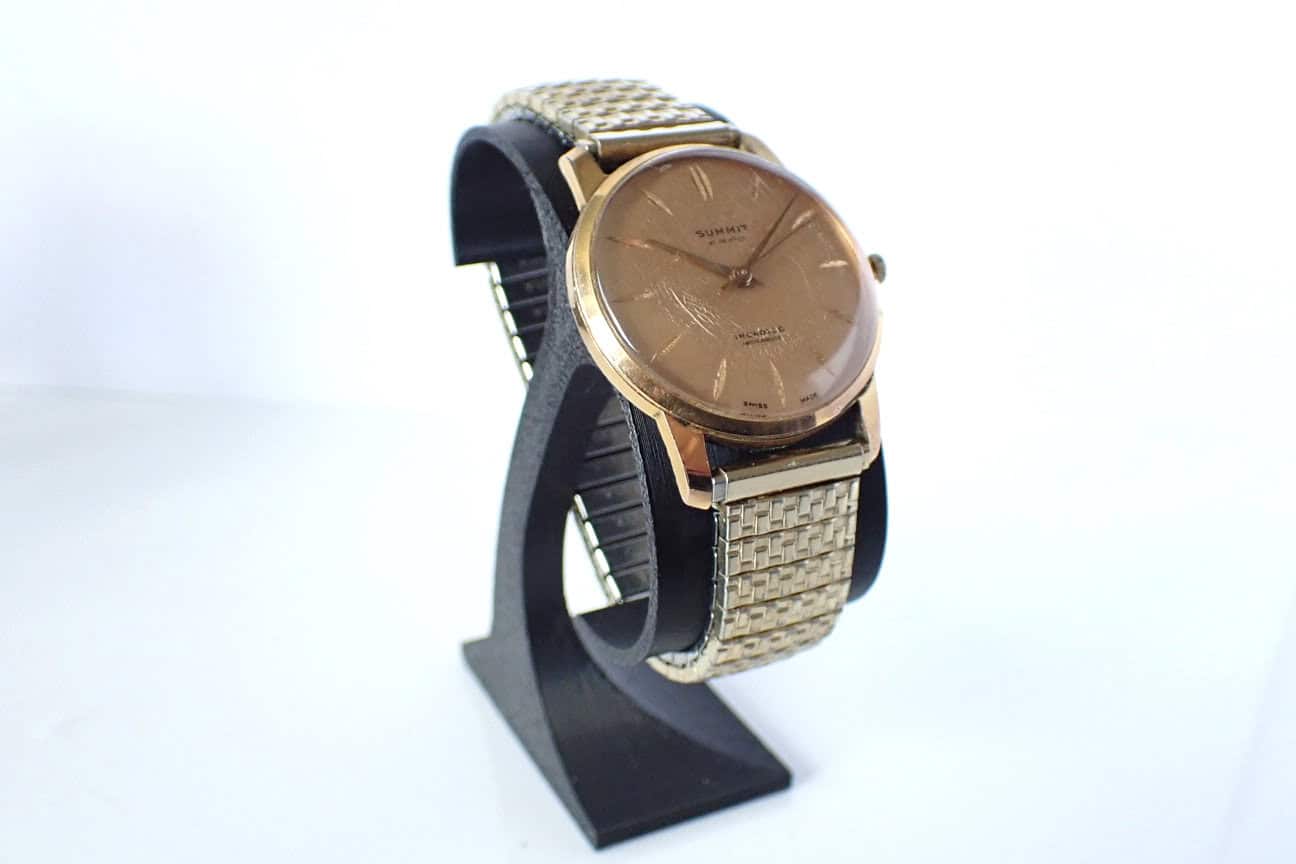 Gold vintage wristwatch with stainless steel mesh bracelet displayed on a black stand.