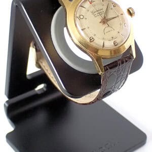 Elegant vintage gold Geneva automatic wristwatch with leather strap on black watch stand.