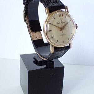 Vintage black leather strap wristwatch with classic design, gold-tone case, and Swiss movement.