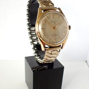 Vintage gold wristwatch with a metal bracelet on black display stand.