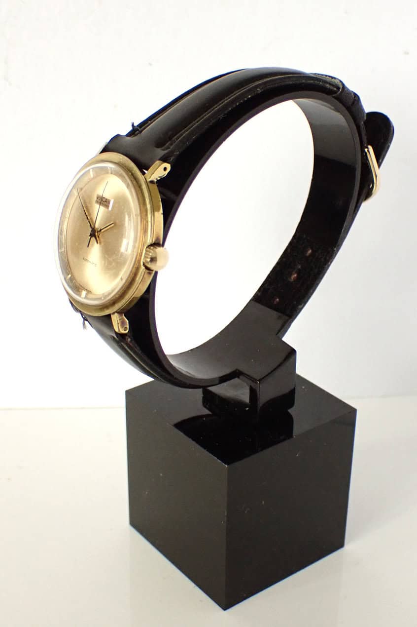 Vintage Vulcain gold-tone men's wristwatch with black leather strap on display stand, elegant luxury timepiece.