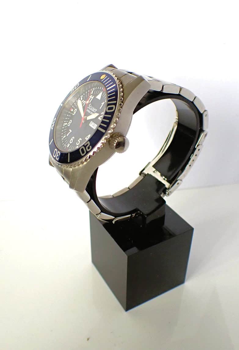 Men's diver watch with black bezel and stainless steel bracelet, displayed on black stand.