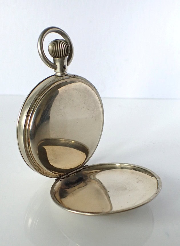 Vintage silver pocket watch in open case, classic travel accessory.