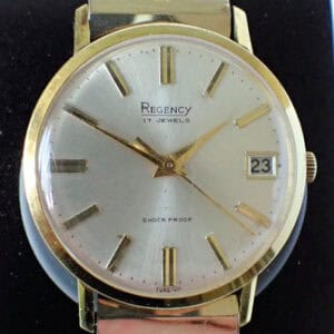 A Regency 17 Jewels 1970s Gold Plated Mechanical wristwatch with a silver dial, marked "17 Jewels" and "Shock Proof," shows the time as 10:08 with a date window set to 23.