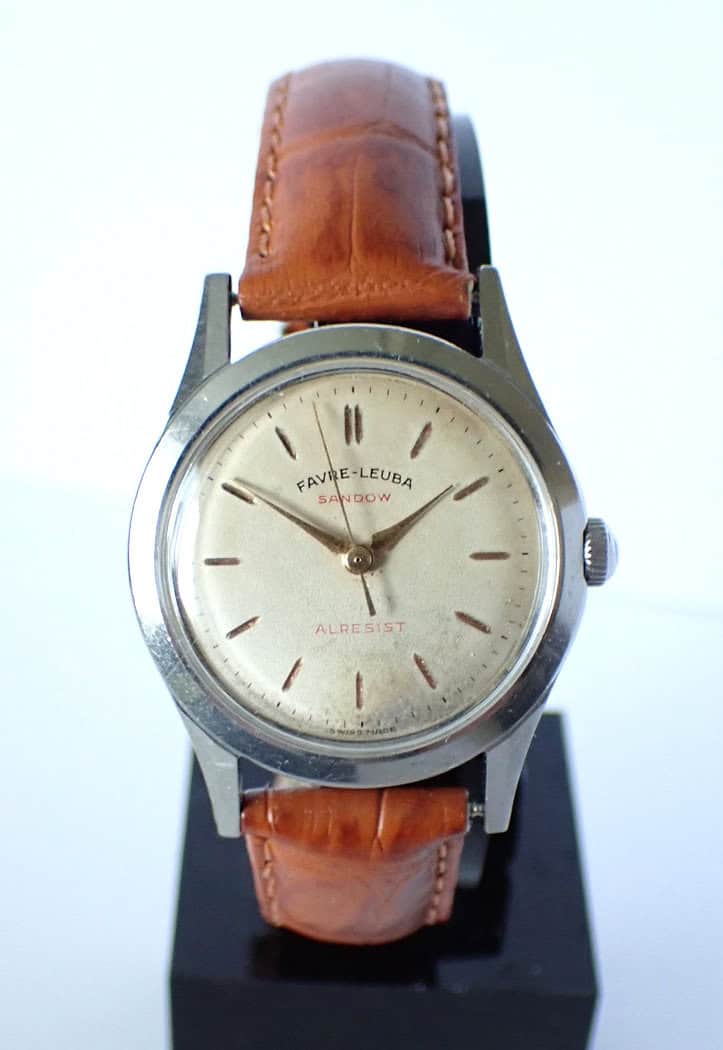 A vintage Favre Leuba Sandow 'Allresist' mechanical 1950s wristwatch with a round silver dial, simple hour markers, and a brown leather strap, displayed on a black stand.