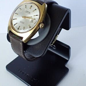 Vintage Movado men's wristwatch with gold-tone case and leather strap on watch stand.