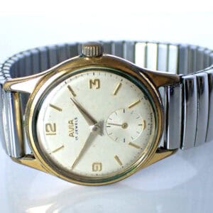 Avia 15 Jewels Mechanical late 1940s wristwatch featuring a round gold-tone case, white dial with gold hour markers, small seconds sub-dial, and a silver metal expanding bracelet.