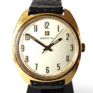 The Zenith Gold Tone Automatic Watch C1977 features a gold round case, white dial with black Arabic numerals and hands, a black leather strap, and the Zenith logo below the 12 o’clock mark.