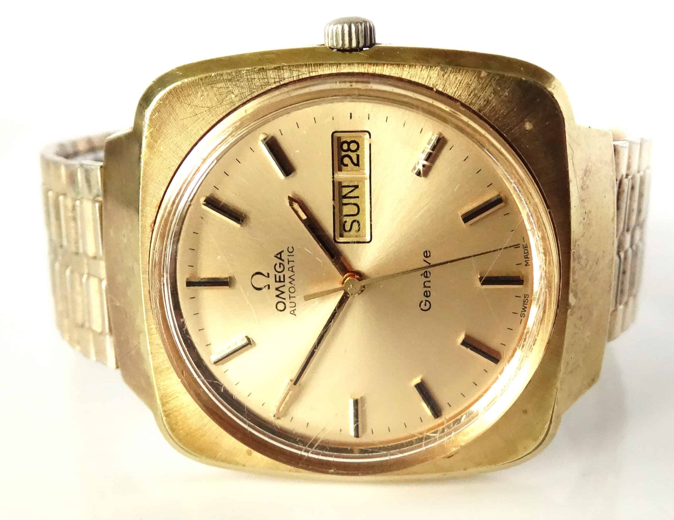 A vintage Omega Day Date Genève Automatic Watch c.1973 with a square gold case, metallic strap, and champagne dial displaying day and date in English. The hands show about 3:58.