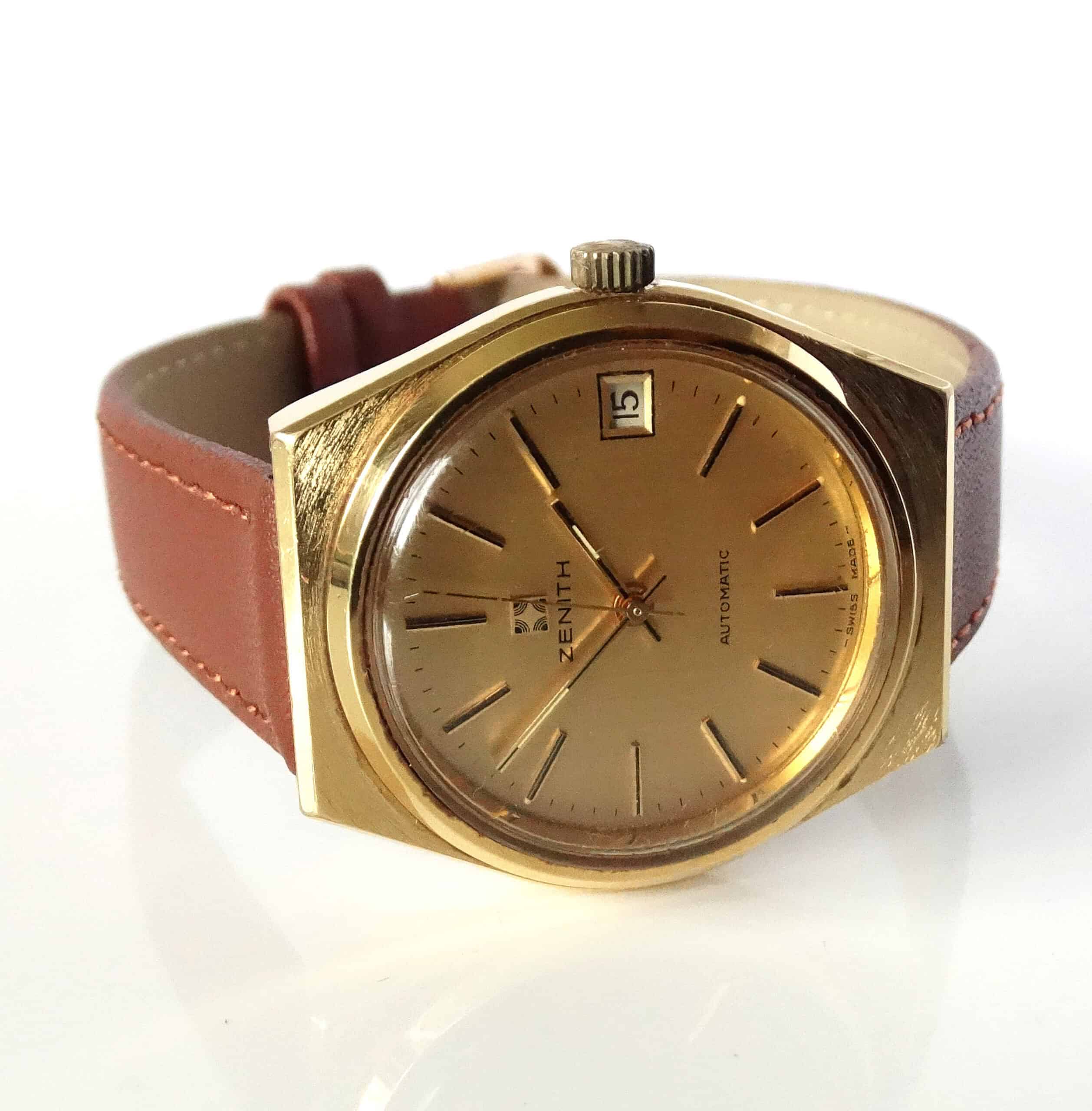 A Zenith Date Automatic Watch Calibre 2572 c1976 with a gold case, gold dial, brown leather strap, and date set to the 15th is shown on a white background.