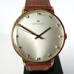 A Hamilton Mechanical Dress Watch c1975 featuring a round silver dial, gold markers, brown leather strap, and two hands, photographed against a plain background.
