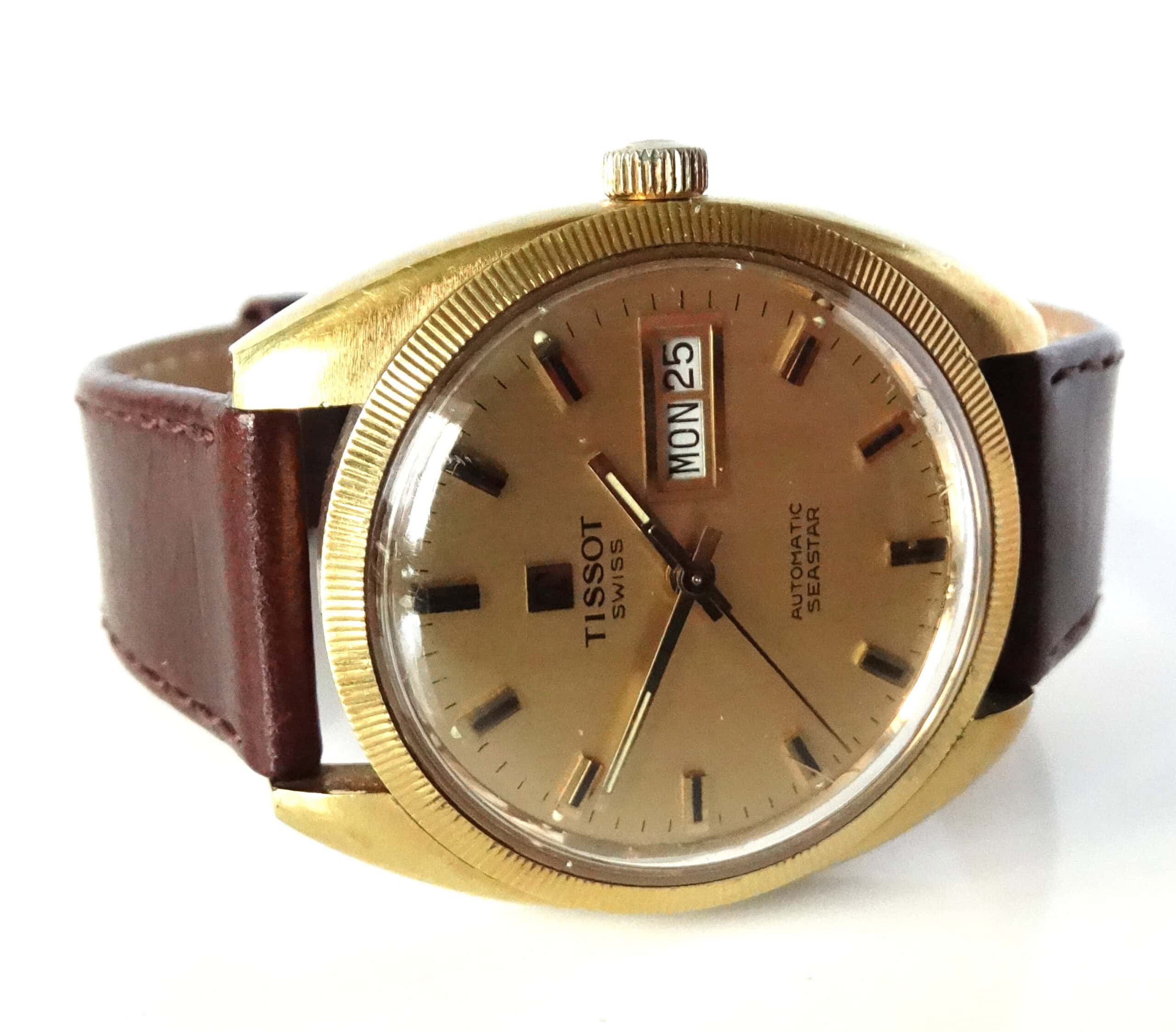 A vintage Tissot Seastar Day Date Automatic c1975 wristwatch features a gold-tone round case, brown leather strap, and a gold dial with day-date display showing WED 25.