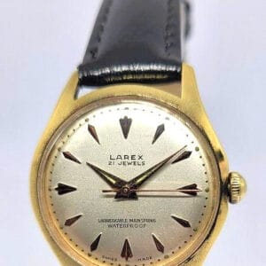 The Larex 21 Jewels Gold-Plated Mechanical Watch (1960s) features a gold case, black leather strap, silver dial with triangular hour markers, displaying "21 Jewels," "Unbreakable Mainspring," and "Waterproof" on the face.