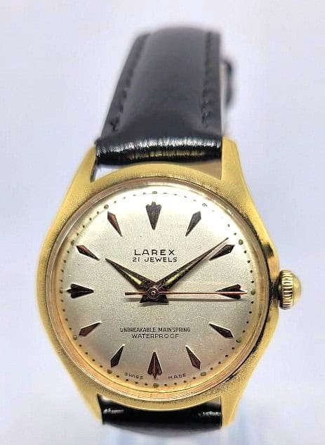 The Larex 21 Jewels Gold-Plated Mechanical Watch (1960s) features a gold case, black leather strap, silver dial with triangular hour markers, displaying "21 Jewels," "Unbreakable Mainspring," and "Waterproof" on the face.