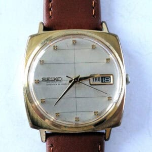 The SEIKO Sea Lion M88 Diashock is a vintage automatic day-date watch with a square gold-tone case, brown leather strap, silver dial displaying THU 18, gold hour markers, and black hands.