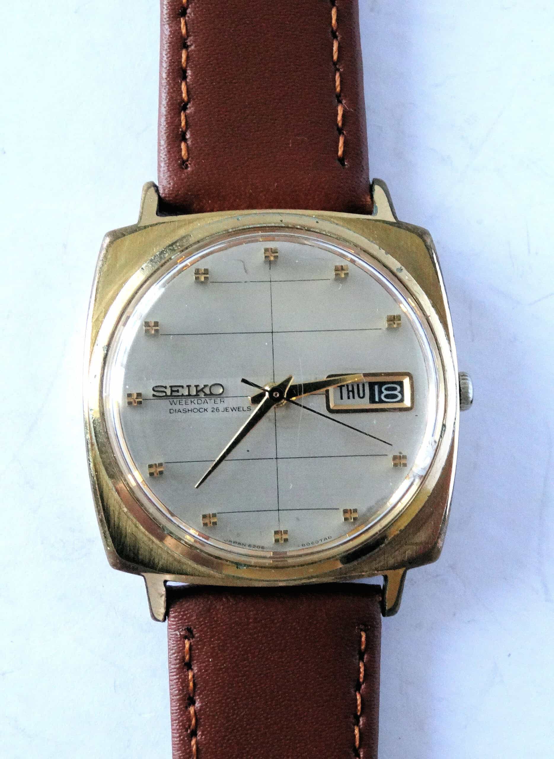 The SEIKO Sea Lion M88 Diashock is a vintage automatic day-date watch with a square gold-tone case, brown leather strap, silver dial displaying THU 18, gold hour markers, and black hands.