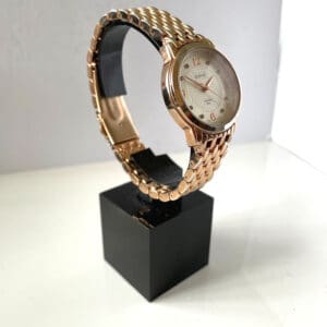 The August Steiner Diamond Silver Dial Ladies' Watch AS8133RG, featuring a gold linked strap and gold hour markers and hands, is displayed on a black rectangular stand against a white background.