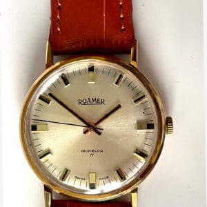 A vintage Roamer Boxed 9ct Presentation Watch circa 1975 with a gold case, white dial, brown leather strap, silver markers, black hands, and "ROAMER" plus "INCABLOC 17 SWISS MADE" on the face. Pay interest-free in three with Klarna.