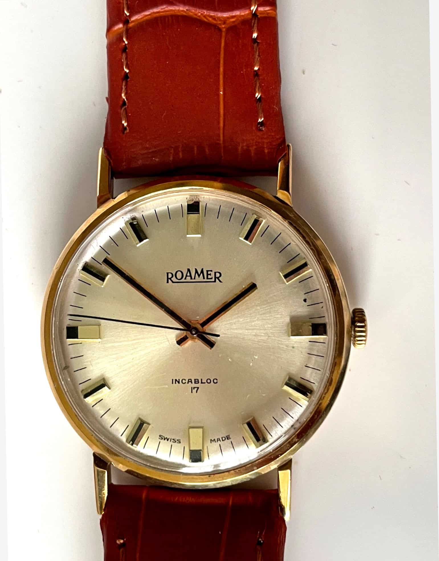 A vintage Roamer Boxed 9ct Presentation Watch circa 1975 with a gold case, white dial, brown leather strap, silver markers, black hands, and "ROAMER" plus "INCABLOC 17 SWISS MADE" on the face. Pay interest-free in three with Klarna.