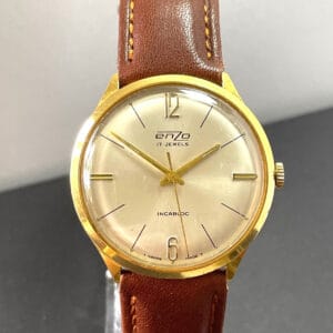 The Enzo 17 Jewel Mechanical Watch features a gold case, light brown leather strap, cream dial with gold markers and thin hands. The watch displays 12:06 and has "17 Jewels" and "Incabloc" on the face.