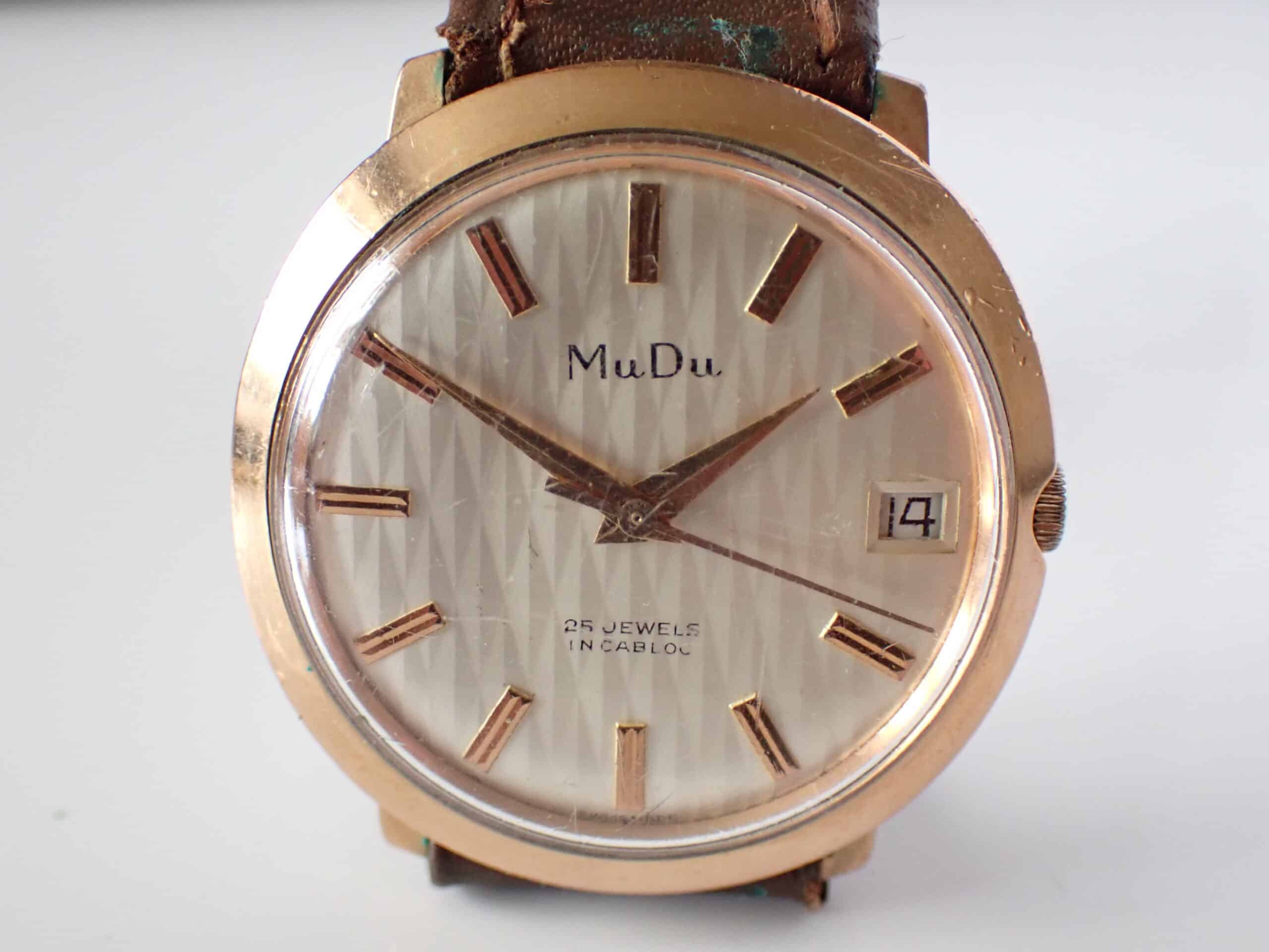 The MUDU Doublematic 25 Jewels Automatic features a gold case, textured white dial with gold hour markers, date window at 14, and brown leather strap. Pay interest-free in three instalments with Klarna.