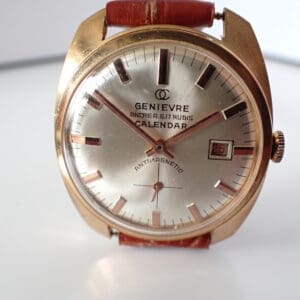 A close-up of the Genievre Ancre A G 17 Rubis Calendar Watch features a gold case, brown leather strap, silver dial, black hour markers, and a date display reading "25," with "CALENDAR" and "ANTIMAGNETIC" on the face. Pay in three with Klarna.