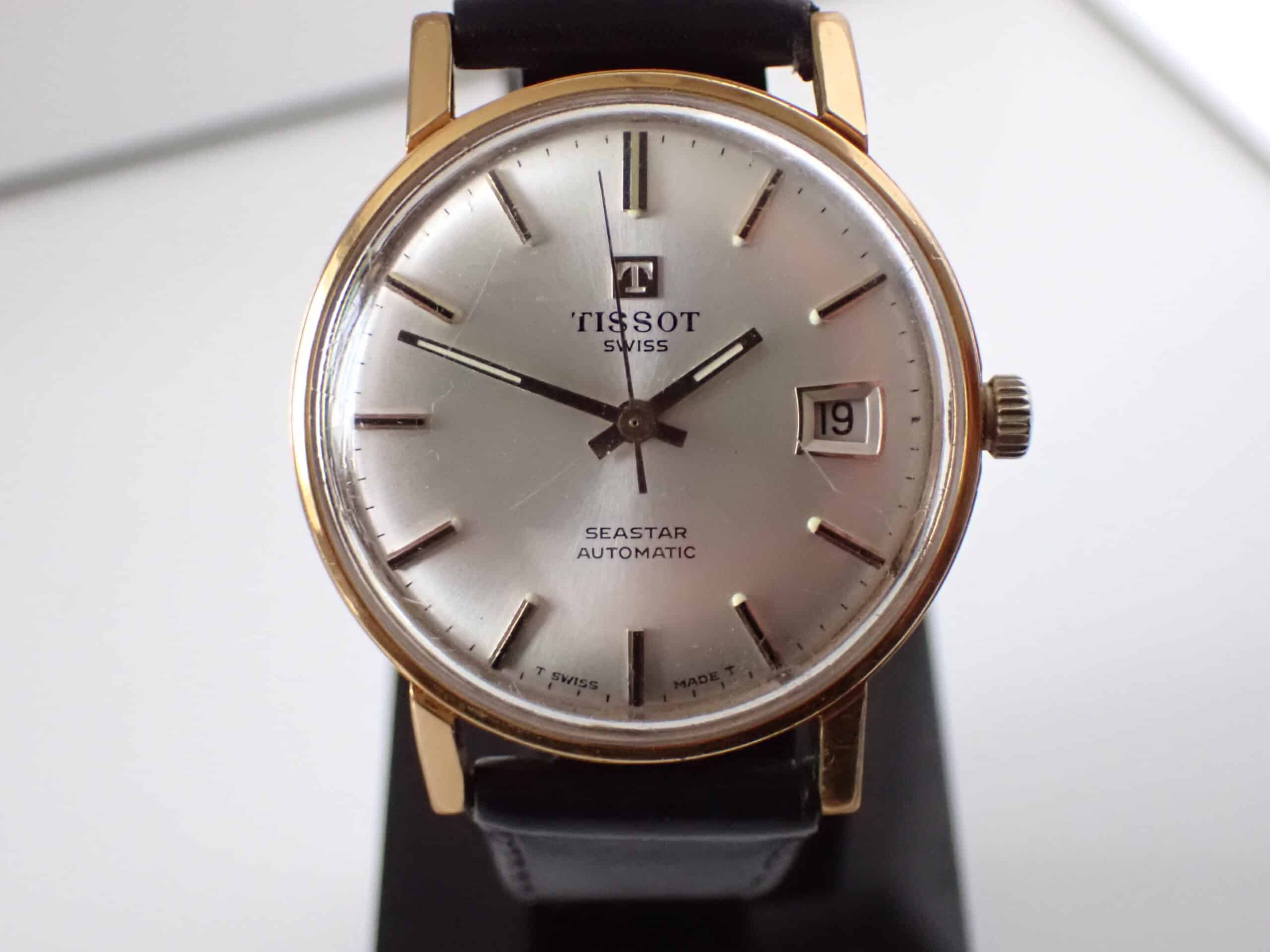 A close-up of the Tissot Seastar Automatic Gold-Plated 1970s Watch, featuring a silver dial, gold-plated case, black leather strap, date display at 19th, and silver hour markers and hands. Available to pay with Klarna.