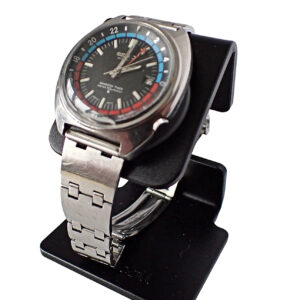 The Seiko NAVIGATOR TIMER Automatic Watch features a silver metal strap, round black dial with red and blue accents, and is shown on a black stand against a white background. Pay interest-free in three with Klarna!.