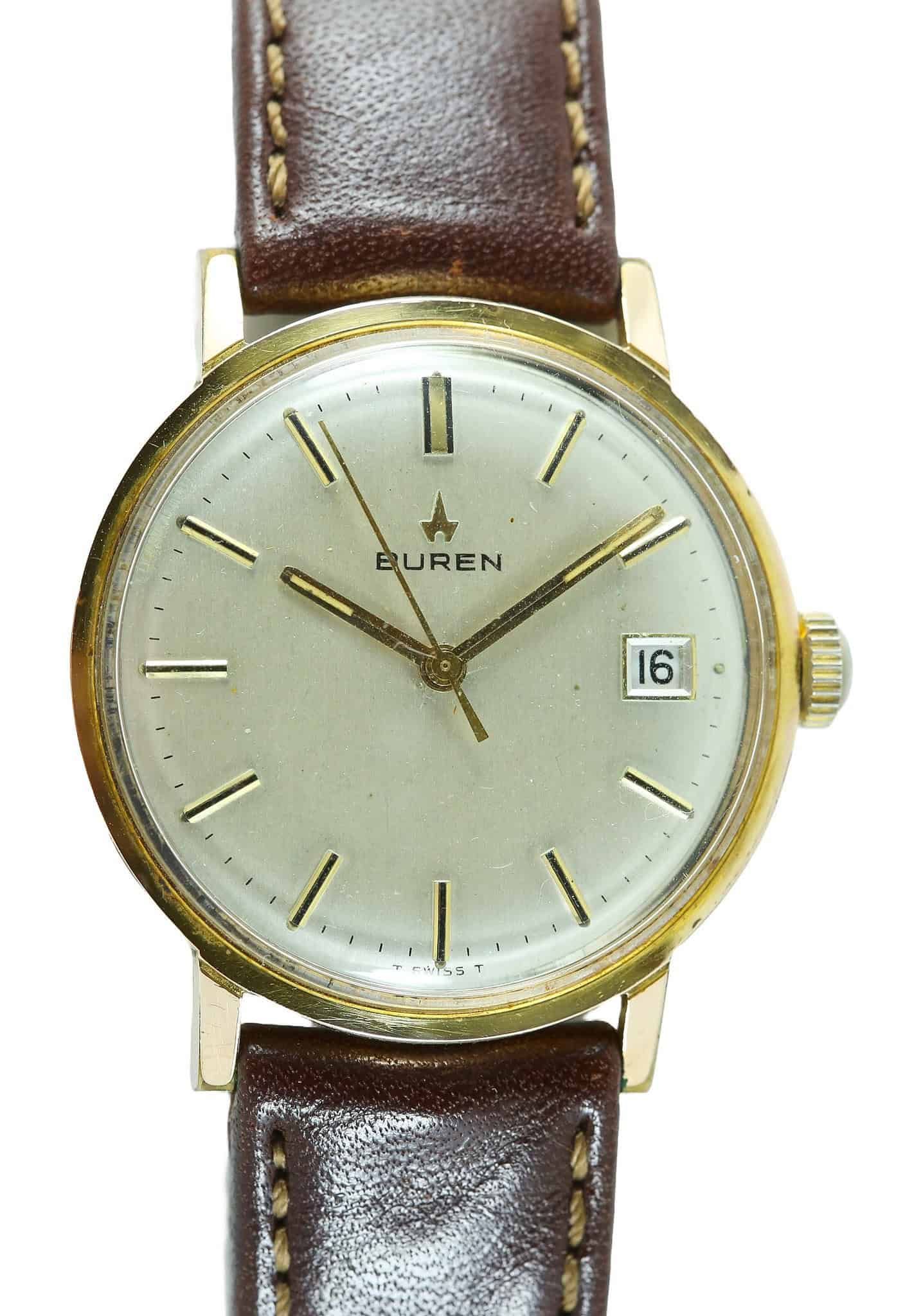 The Buren Mechanical Date Watch features a gold case, white dial with black markers, date window at 3 o’clock, and brown leather strap. Pay interest-free in three with Klarna. The hands are set to 8:19.