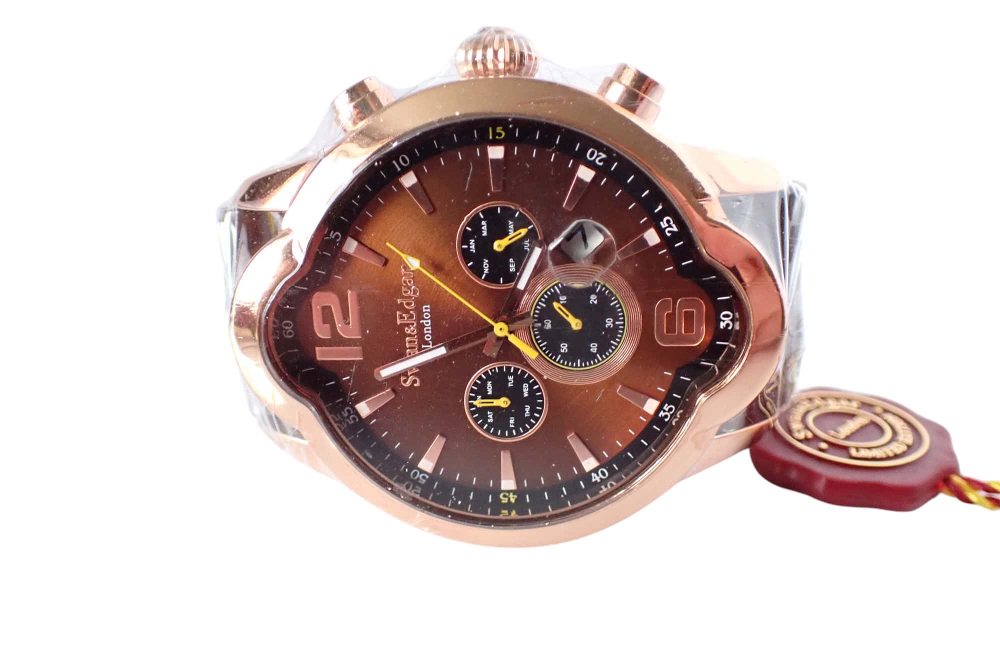 A close-up of the sold-out Swan and Edgar Elliptical Automatic Chronograph shows a brown dial with three sub-dials, gold accents, and a gold case. The new watch has protective plastic, a red tag, and displays the time at about 10:08.