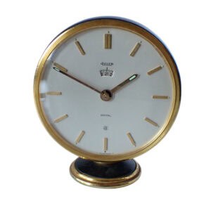 A Jaeger-LeCoultre 8-Day Table Clock, Recital Alarm with a 24-hour scale, features a white dial, gold accents, minimal markers, and is mounted on a small gold and black base. Pay later with Klarna.