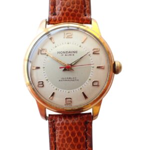 The Mondaine Hand Wind Watch features a brown textured leather strap, gold casing, white dial with gold hour markers and hands, a red second hand, and displays "Mondaine 17 Rubis" on the face.