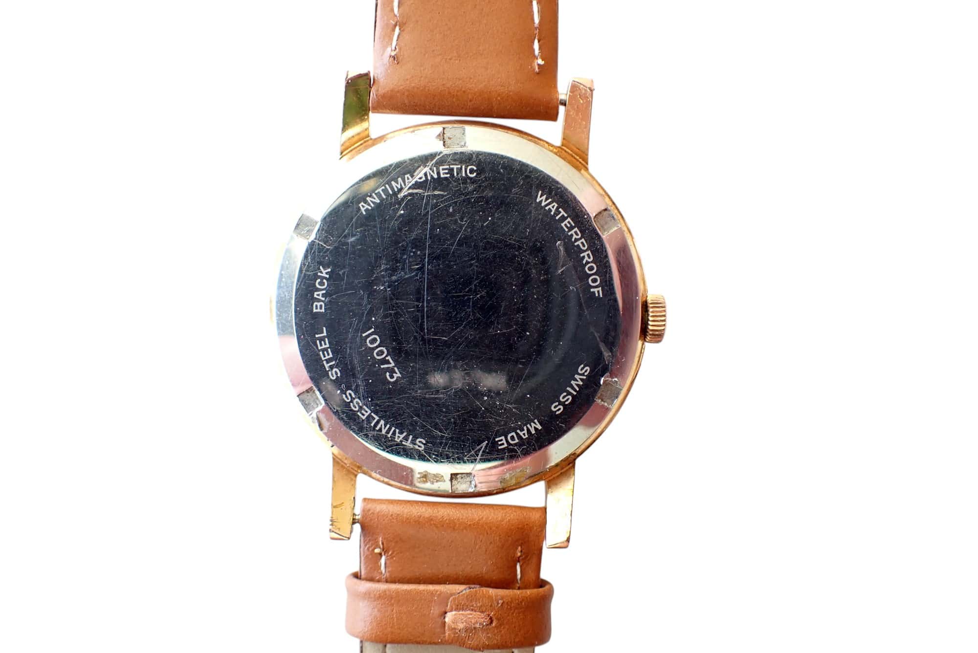 Scratched vintage wristwatch with brown leather strap, waterproof and anti-magnetic features.